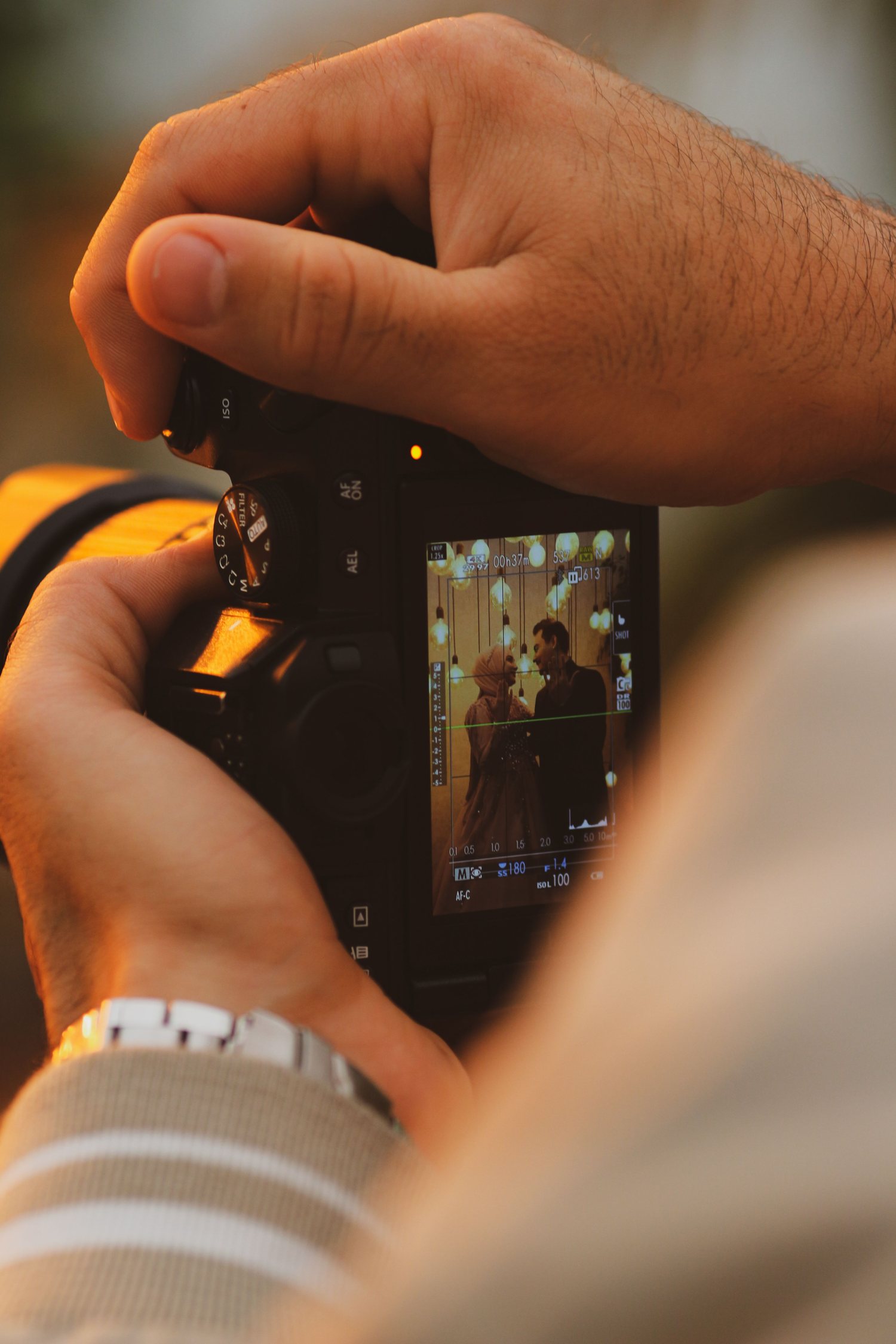 A photographer's hands on a camera, a couple laughing on the screen